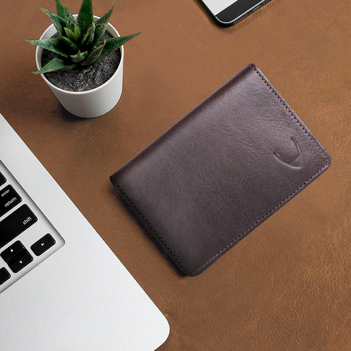 Brown leather bifold wallet placed on desk beside laptop, smartphone and small plant flat lay setup.