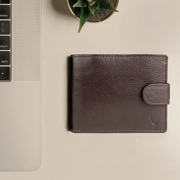 Brown leather Hidesign wallet placed beside a laptop & a plant on a clean, minimal workspace setup.